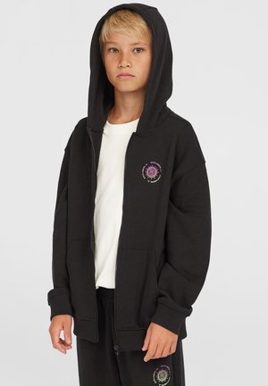 Schwarze Kapuzenjacke aus weichem Material, mit einer Vordertasche und einem bunten Grafikdesign auf der linken Brust. Darunter ein schlichtes weißes T-Shirt.