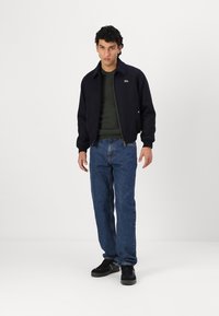 Tumes navy bomber-jakk üle rohelise sviitri, koos siniste teksade ja mustade tossudega. Jakk on varustatud ees oleva lukuga ja kaelusega.