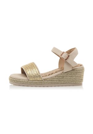 Sandalias de cuña beige con una tira texturizada dorada, hebilla ajustable en el tobillo y suela de yute trenzado. Parte superior de piel suave y plantilla acolchada.