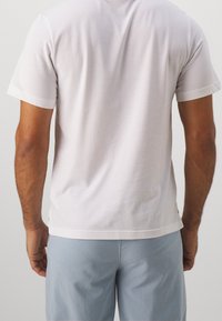 En enkel vit bomullströja med korta ärmar, rund hals och rak nederkant, bärs med ljusblå shorts. Slät textur.