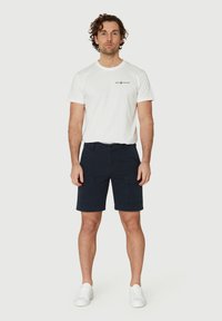 T-shirt en coton blanc avec un logo noir, associé à un short cargo bleu marine foncé avec des poches latérales, et des baskets blanches.