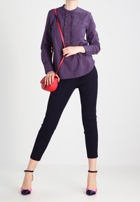 Chemise violette à boutons avec un motif à carreaux, pantalon slim noir et talons avec accents roses. Comprend un petit sac bandoulière rouge.