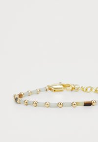 La pulsera con acentos dorados presenta cuentas redondas y rectangulares en tonos azul pálido y marrón, intercaladas con esferas doradas brillantes y un cierre de langosta.