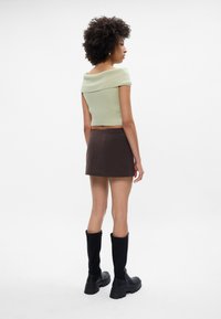 Top corto acanalado menta con diseño de hombros al descubierto, combinado con una falda mini marrón a rayas. Bota alta negra hasta la rodilla completa el atuendo.