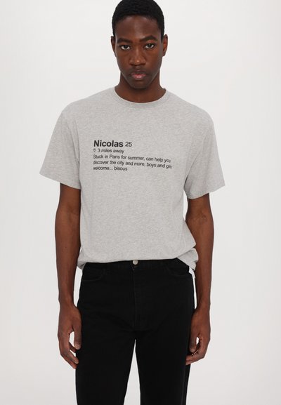 Gray cotton t-shirt with printed text in black. Crew neck, short sleeves. Paired with black jeans. Simple, casual design.