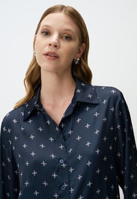 Navyblauwe zijden blouse met een puntkraag, voorzien van delicate bloemenpatronen in wit en rood. Twee knopen zichtbaar bij de kraag.