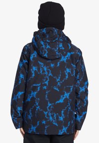 Vattentålig jacka med svart tyg och ett blått blixtmönster, justerbar huva och långa ärmar med elastiska muddar.