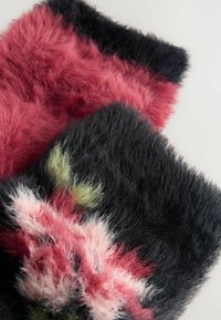 Soft, fluffy fabric with black, pink, red, and green colors, arranged in overlapping sections on a light background.