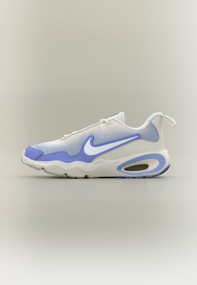 Λευκό και ανοιχτό μωβ αθλητικό παπούτσι Nike με επενδεδυμένη σόλα και λογότυπο Swoosh, εμφανιζόμενο από δεξιά πλευρά σε απλό φόντο.