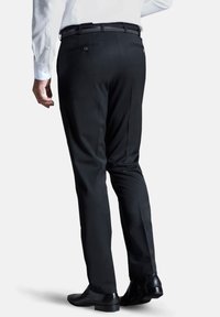 Schwarze, maßgeschneiderte Hose mit glatter Oberfläche, ausgestattet mit zwei Gesäßtaschen und einem schlanken Schnitt. Getragen mit einem weißen Hemd.