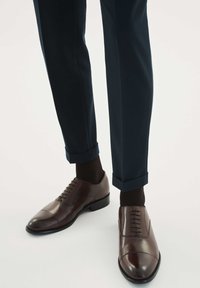 Scarpe eleganti da uomo in pelle marrone con punta arrotondata, design con lacci e cuciture a contrasto. Indossate con pantaloni scuri e calzini scuri.