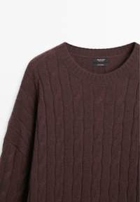 Maglione in cashmere a maglia cable marrone scuro con collo rotondo e etichetta del marchio visibile all'interno del colletto su sfondo bianco.