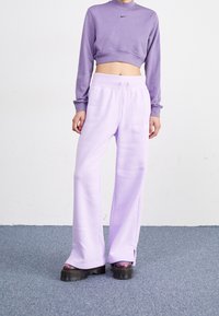 Person med lavendelcroppad sweatshirt och matchande vida sweatpants med svarta platåskor som står på en matta.