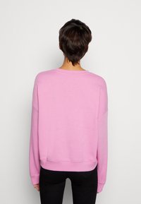 Sudadera rosa claro con corte relajado, escote ancho y mangas largas. Textura suave y puños acanalados en el dobladillo.