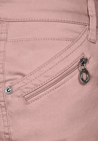 Růžové bavlněné kalhoty s přední kapsou na zip, stříbrnými detaily a kontrastním prošíváním. Hladká textura po celé ploše.