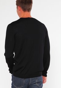 Maglione nero con collo a giro e maniche lunghe, realizzato in un materiale leggero, caratterizzato da una texture semplice e un design aderente.
