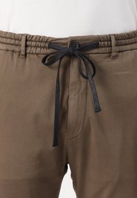 Brune bukser med elastisk talje og sort snor, front knaplukning og glat stoftekstur.