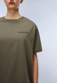 Oliivinvihreä puuvillapaita, jossa on lyhyet hihat ja pyöreä kaula-aukko. Rinnassa on brodeerattu "NAPAPURI" -logo. Pehmeä rakenne, rento istuvuus.