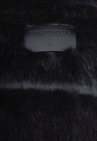 Un matériau en fourrure noire avec une étiquette en cuir mat embossée du texte "PATRIZIA PEPE". La texture est douce avec des poils plus longs et une finition en cuir lisse.