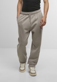 Hellgraue Jogginghosen mit elastischem Bund und Kordelzug, ausgestattet mit Seitentaschen und einem kleinen roten Logo am linken Oberschenkel.