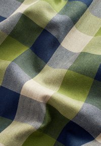 Gros plan d’un tissu avec un motif tissé texturé en plaid vert, bleu marine, beige et gris.
