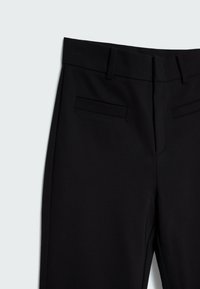 Pantalon noir sur mesure avec passants de ceinture, deux poches avant à double passepoil et une fermeture éclair avant dissimulée sur un fond gris clair.