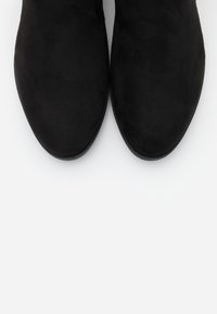 Bottines en suede noir avec une texture lisse et un bout rond, dotées d'un design minimaliste et d'une semelle en caoutchouc plate.
