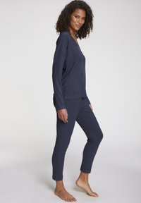 Navy loungewear set with a ribbed texture; features a V-neck long-sleeve top and slim-fit pants with long, fitted cuffs. Bare feet visible.