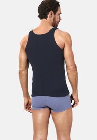Black tank top with a round neckline, fitted design, and smooth texture, paired with gray boxer shorts. Back view of the outfit.