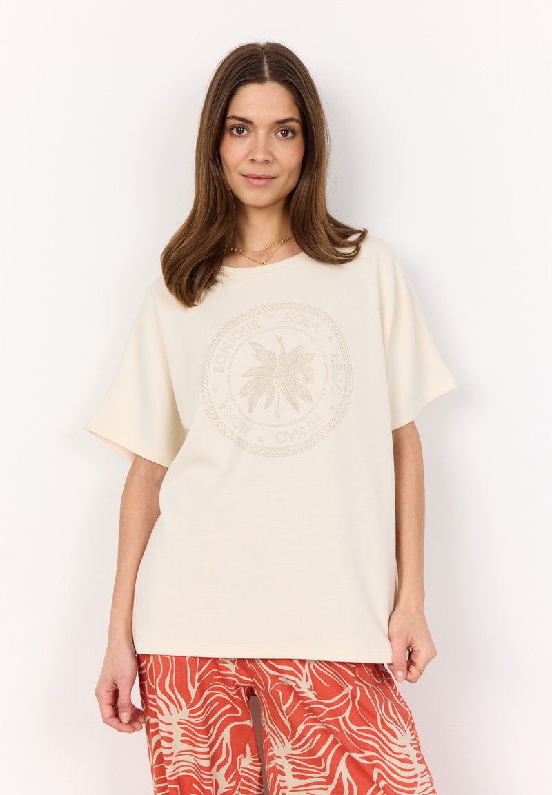 Cream short-sleeve T-shirt with a circular palm tree graphic and text in a tonal print; worn with red patterned pants.