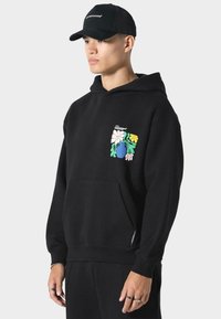 Mustapaita, jossa on etutasku ja värikäs kukkakuosi vasemmassa rinnassa. Materiaali näyttää pehmeältä ja mukavalta.