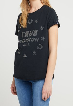 Zwart katoenen T-shirt met sprankelend zilveren "TRUE RELIGION"-tekst, omringd door sterren en afgeronde accenten. Korte mouwen, relaxed fit.