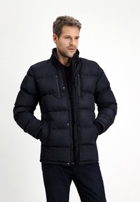 Giacca imbottita nera con colletto alto, chiusura con zip e due tasche sul petto. Caratterizzata da un motivo a quadri orizzontali e una texture liscia.