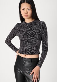 Dugi rukav crop top u crnoj boji s metalik uzorkom zebra, koji ima uski kroj i suptilne puf rukave, u paru s kožnim hlačama.