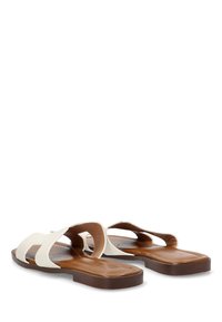 Sandalias planas con una parte superior de goma blanca que presenta un diseño de tiras en cruz y suelas de goma marrón. Textura suave sin patrones adicionales.
