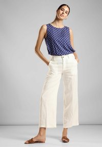 Top senza maniche blu con motivo a diamante, abbinato a pantaloni beige a gamba larga e sandali marroni con fascia. Tessuto morbido ben visibile.