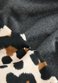 Leopardmønsteret stof i creme med sorte og brune pletter, lagt over et blødt, mørkegråt tekstil. Begge materialer har en tekstureret overflade.