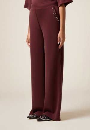 Bordeaux wijde broek gemaakt van zacht materiaal met decoratieve versieringen aan de zijkant. Gecombineerd met puntige zwarte schoenen.