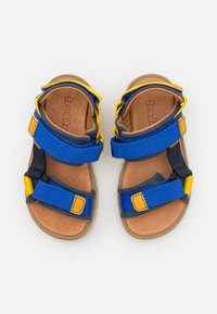 Blå og gule åpne sandaler med justerbare stropper og teksturerte såler. Brun såle og polstret design for komfort og fleksibilitet.