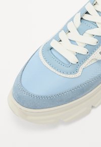 Lys blå sneakers med en blanding av glatt nylon og semsket skinn, med hvite lisser og sømdetaljer, samt en tykk hvit såle.