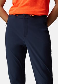 Pantalon d'extérieur bleu marine en tissu léger. Comprend une poche zippée, une taille élastique avec cordon de serrage et un design devant plat.