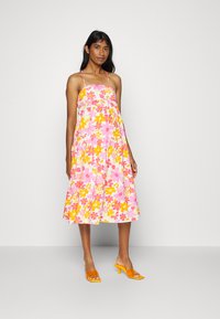Vestido midi floral com cores rosa, amarelo e branco. Apresenta alças finas e cintura franzida. Combinado com saltos abertos cor de laranja.
