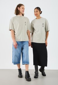 Helles graues übergroßes T-Shirt mit Frontdesign, kombiniert mit einem langen schwarzen Rock und blauen Denim-Shorts, getragen mit schwarzen Kampfstiefeln.
