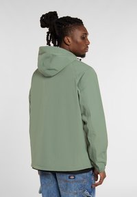 Lysgrøn hættejakke lavet af letvægtsmateriale, med et enkelt design, elastiske manchetter og lige kant, båret over blå jeans.