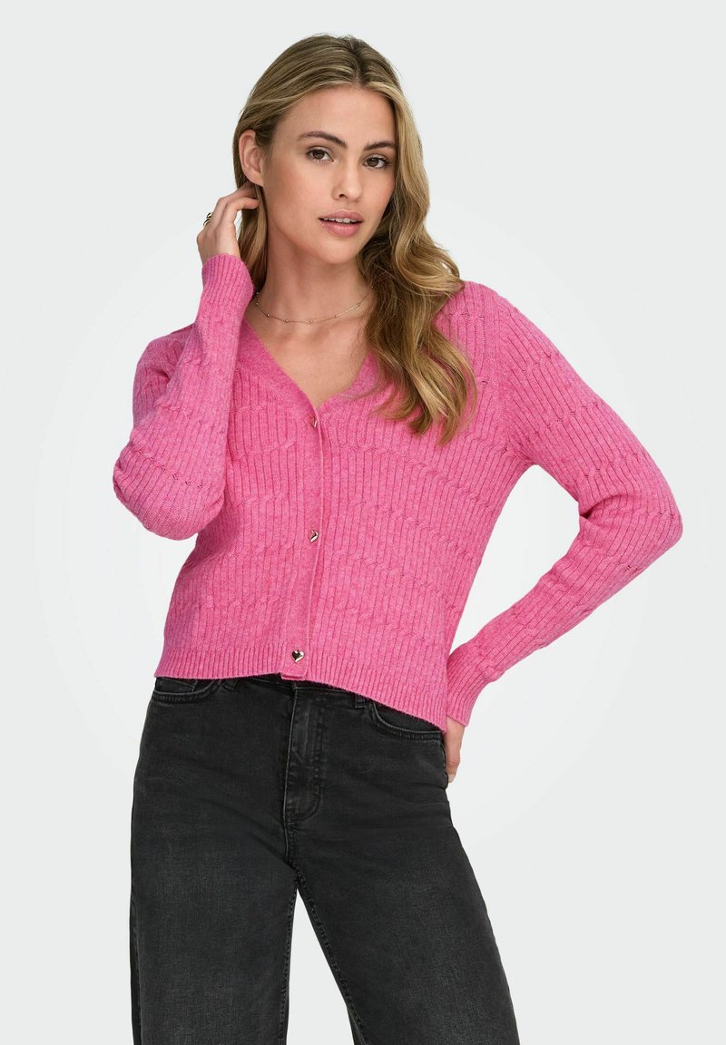 Cardigan rosa fucsia a maglia con scollo a V, texture a coste e dettagli di bottoni a forma di cuore, abbinato a pantaloni neri.