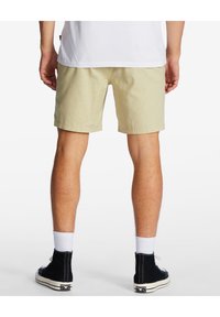 Shorts beiges en tissu texturé, avec un devant plat et un ourlet retroussé, associés à des baskets montantes noires et des chaussettes blanches.