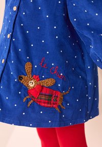 Chemise en velours côtelé bleu à pois blancs, avec un motif brodé d'un chien portant une écharpe à carreaux rouges et le texte "le Chien".