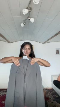 Gray blazer with notch lapels, single button closure, and long sleeves, displayed on a hanger. Smooth fabric with subtle texture.