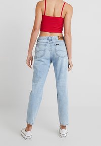 Kvinna som bär ljusblå högmidjade jeans, vita sneakers och en röd kort topp, stående med ryggen mot kameran.