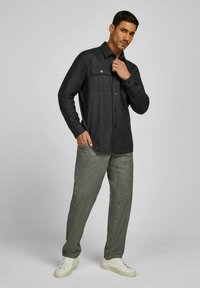 Dunkelgraues langärmeliges Hemd mit Knopfleiste und zwei Brusttaschen, kombiniert mit strukturierten hellgrauen Hosen und weißen Sneakers.